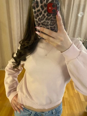 Ljusrosa sweatshirt med ribbade muddar - Säljer en ljusrosa sweatshirt med rund hals och ribbade muddar vid ärmslut och nederkant. Tröjan har en clean look utan tryck eller mönster, och är tillverkad i mjuk bomullsmix. Perfekt för chill dagar och enkel att matcha med jeans eller leggings.