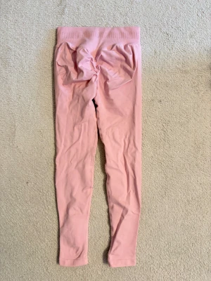 Rosa leggings med hög midja - Snygga ljusrosa leggings med bred, ribbad midja som sitter skönt och ger extra stöd. Modellen är tight och följer kroppen, perfekt för träning eller chill. Materialet känns mjukt och stretchigt, vilket gör dem riktigt bekväma att ha på sig.