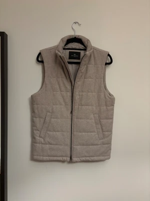 Vest från John Henric - Stilren beige dunväst från John Henric. Västen är köpt i somras men använd typ 1 gång inomhus, den är fläckfri. Storlek S. Köptes för 1600 tror jag. Skriv vid frågor eller funderingar!