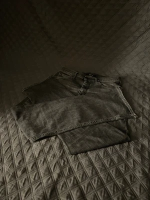 Svarta Replay jeans  - Säljer ett par svarta jeans från Replay med snygg tvättad look och raka ben. Klassisk femficksmodell med tydliga sömmar och Replay-märke bak i midjan. Jeansen är i jeansmaterial och har en cool, lite sliten finish. Och är i st w26