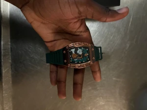 Richard Mille grön klocka med roséguld - Säljer en Richard Mille klocka med grön gummirem och en cool roséguldfärgad boett. Urtavlan har synliga mekaniska detaljer och en unik form som sticker ut. Perfekt för dig som gillar exklusiv design och vill ha något som verkligen syns på handleden.