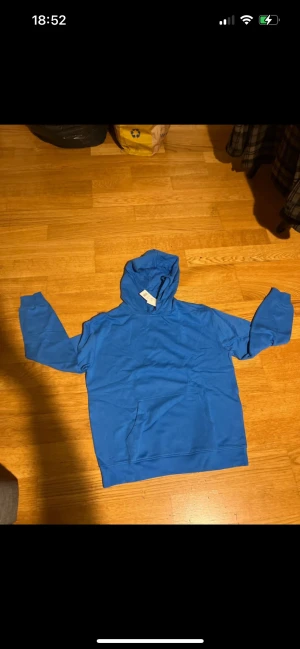 Blå hoodie från Cubus i bomull - Snygg blå hoodie oanvänd med etiketten från Cubus i storlek M. Tröjan har luva med snörning, magficka och är tillverkad i mjuk bomull. Perfekt för chill dagar och enkel att matcha med jeans eller joggers. Färgen är klar blå och modellen är klassisk med lång ärm.
