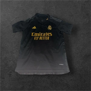 Real Madrid Rodrygo 11 svart matchtröja - Snygg svart Real Madrid fotbollströja från Adidas med guldiga detaljer och tryck. Framsidan har klubbmärke och Emirates Fly Better, baksidan har Rodrygo och nummer 11 i guld. Kortärmad modell i lätt funktionsmaterial med Aeroready-teknologi. Storlek S men funkar även för M.