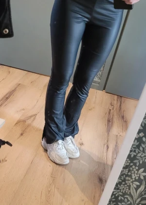 Svarta bootcut byxor från Shein XS - Säljer ett par svarta bootcut byxor från Shein i storlek XS. Byxorna har en glansig finish, elastisk midja och är tillverkade i syntetmaterial. Snyggt utsvängda ben med slits nedtill för extra edge.