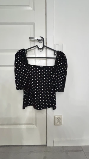 Svart prickig blus med puffärm - Supersöt svart blus från Gina Tricot med vita prickar och puffiga trekvartsärmar. Toppen har en fyrkantig ringning och är figurnära i modellen. 