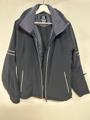 Svart skidjacka från Salomon, XL - Svart snygg skidjacka i mycket bra kvalitet från Salomon. Snygga vita detaljer och logga på ärmen. Vattentät och 4-vägs stretchtyg. Otroligt skön med full rörelsefrihet. Primaloftisoleringen gör jackan mycket varm. Snölås. Nästan oanvänd. 