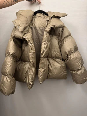pufferjacka med stor krage - Säljer en pufferjacka med oversized passform och stor krage. Jackan har långa ärmar och är tillverkad i glansig syntet med quiltade partier. Perfekt för kalla dagar när du vill ha en riktigt snygg look.