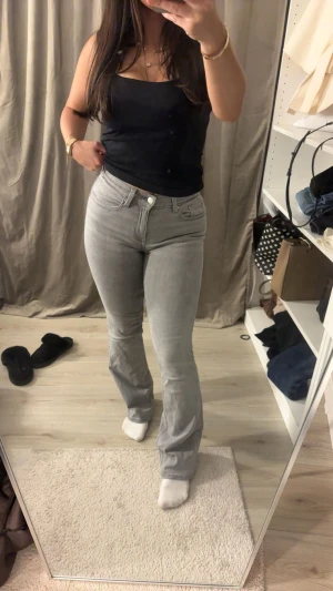 Grå bootcut jeans från Gina Tricot (Perfect Jeans) - Snygga grå jeans från Perfect Jeans i storlek 32. Modellen har bootcut-ben och normal passform med klassisk femficksdesign. Jeansen är tillverkade i mjukt denim-material och har mellan hög midja för en schysst siluett. Perfekt för dig som gillar stilrena och bekväma jeans.