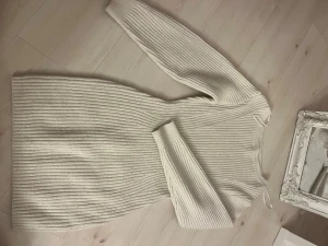 Beige ribbad stickad klänning - Säljer en beige stickad klänning med ribbad struktur och lång ärm. Klänningen har en enkel, rak passform och är perfekt för dig som gillar en clean och cozy look. Materialet är mjukt och värmande, och färgen är neutral vilket gör den lätt att matcha.