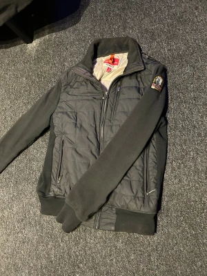 Svart quiltad jacka från Parajumpers - Svart jacka från Parajumpers med quiltad front och rygg, mjuka ärmar och ribbade muddar. Snyggt broderat PJS-märke på ärmen och dragkedjor på fickorna. Insidan är fodrad med ljusgrått tyg