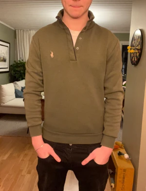 Polo Ralph Lauren tröja - Snygg olivgrön polotröja från Ralph Lauren med klassisk broderad logga på bröstet. Tröjan har lång ärm och en halv knappslå vid halsen. Nypris ca 1500.  Priset är inte hugget i sten, så kom gärna med förslag! Om du har några frågor är det bara att höra av dig!