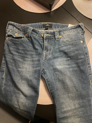 True Religion Joey Low Rise Flare Jeans - Säljer ett par blåa jeans från True Religion, modell Joey Low Rise Flare. De har snygga kontrastsömmar, klassiska fickor och guldfärgade knappar. Jeansen har låg midja och utsvängda ben!!💓💓Säljs för de ej kommer till användning💞(Använda max 2 gånger)