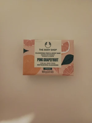 The Body Shop Pink Grapefruit Soap Bar - Fräsch rengöringsbar för ansikte och kropp från The Body Shop med doft av pink grapefruit. Vegansk och passar alla hudtyper. Snyggt förpackad med rosa och orange grapefruktmotiv, 100g. Perfekt för dig som gillar fruktiga och uppiggande produkter.