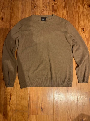 Beige rundhalsad tröja Oscar Jacobson - Snygg beige rundhalsad tröja från Oscar Jacobson, modell Valter Roundneck. Tillverkad i Italien med mjukt stickat material och ribbade muddar vid ärmslut och nederkant. Perfekt för dig som gillar stilrena och klassiska plagg.