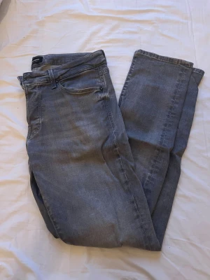 Grå slim jeans från Jack & Jones - Slim Glenn jeans från Jack & Jones i snygg grå tvätt. Modellen har smal passform, klassisk femficksdesign och normal midja. Jeansen är tillverkade i mjukt denim-material med dragkedja och knappstängning. Perfekt för dig som gillar stilrena och moderna jeans.