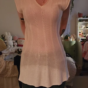 Vit stickad kortklänning med v-ringning - Vit stickad kortklänning med v-ringning och vertikala hålmönster. Figurnära upptill med lätt utsvängd nederdel.