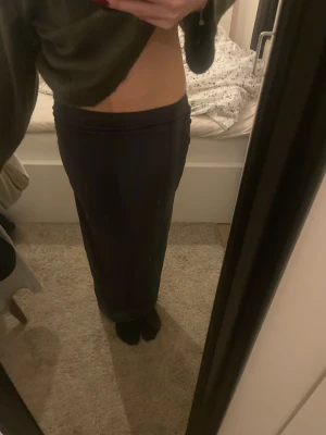 Mörkgrå långkjol med rynkade detaljer - Mörkgrå långkjol med snygga rynkade detaljer på sidan. Kjolen har en rak och tight passform som faller hela vägen ner till fötterna. Perfekt för dig som gillar minimalistisk stil och vill ha en enkel men stilren kjol.