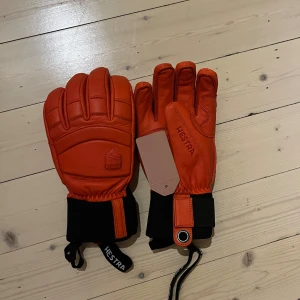 Hestra Alpine Pro orange skinnhandskar - Säljer ett par orangea Alpine Pro handskar från Hestra. De är tillverkade i tåligt skinn med svart mudd och justerbart band vid handleden. Handskarna har broderad Hestra-logga och är riktigt grymma för kalla dagar i backen.