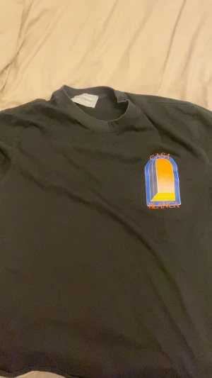 Svart Casa Blanca t-shirt  - Svart t-shirt från Casa Blanca med stort grafiskt tryck i blått, gult, orange och grått på framsidan. Trycket har en cool fönsterdesign och texten 'CASA BLANCA' i orange. Klassisk rund hals och korta ärmar. Materialet är mjuk bomull.