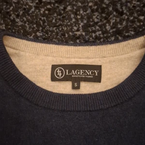 Mörkblå stickad tröja från Lagency - En stilren mörkblå stickad tröja från Lagency i storlek S. Tröjan har rund halsringning, ribbade muddar vid ärmslut och nederkant samt långärmad passform. Perfekt för dig som gillar enkel och klassisk design med en snygg färg.
