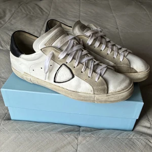 Philippe Model Skor – Storlek 45 - Säljer ett par Philippe Model PRSX Low i storlek 45. Skorna är väl använda men fortfarande i bra och fullt användbart skick, utan större slitningar eller skador. Modellen är känd för sin exklusiva kvalitet, handgjorda detaljer och den ikoniska sköld-loggan på sidan. Färg i vitt med svarta detaljer – stilrent och tidlöst.  Originalkartong ingår, vilket syns på bilderna. Nypris ligger runt 3 500 kr, men varierar beroende på butik.  Pris kan diskuteras!