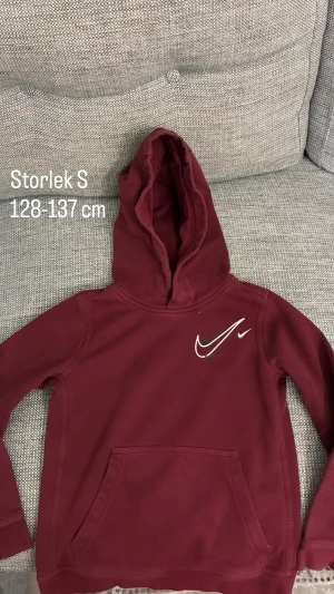 Vinröd Nike hoodie med huva - Snygg vinröd hoodie från Nike med stor huva och klassisk logga i vitt på bröstet. Tröjan har en stor magficka och långa ärmar, perfekt för chill dagar. Mjuk och skön känsla tack vare bomullsmaterialet.