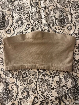 Beige bandeau tubtopp från 157 - Säljer en enkel och stilren beige bandeau tubtopp från 157 i storlek XS/S. Toppen är ärmlös och har en rak, croppad passform som sitter tight mot kroppen. Perfekt att styla med jeans eller kjol för en clean look.