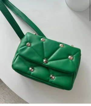 Grön quiltad axelväska med nitar från Zara - Snygg grön axelväska med quiltad design och silverfärgade nitar. Väskan har en rektangulär form och bred axelrem, perfekt för att ge din outfit en cool touch. Materialet är mjukt och har en lyxig känsla.