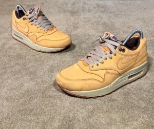 Nike Air Max 1 sneakers EUR 38,5 - Nike Air Max 1 sneakers i beige mocka med grå snörning och ljusgrå sula. Klassisk rund tå och synlig Air-enhet i sulan. Snyggt broderad Nike-logga på hälen och sidan. Insidan är brun och plösen har Nike Air-märke. Perfekt för dig som gillar stilrena och tidlösa sneakers.