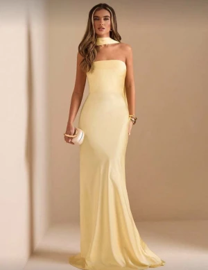 Ljusgul långklänning med scarfdetalj - Säljer en elegant ljusgul långklänning med axelbandslös design och scarfdetalj runt halsen som hänger ner i ryggen. Klänningen har en figurnära passform och är tillverkad i ett slätt, glansigt material som ger en lyxig känsla. Perfekt för bal!