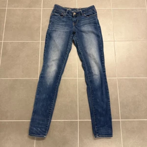 Levi's Demi Curve skinny jeans blå - Snygga blå Levi's Demi Curve skinny jeans med klassisk femficksdesign och gul kontrastsöm. Modellen har smal passform och normal midja, med läderpatch baktill och slitningar på framsidan för en cool look. Storlek 26