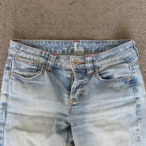 Ljusblå bootcut jeans med broderade fickor - Säljer ett par ljusblå jeans med bootcut passform och klassisk femficksdesign. Jeansen har snygga broderade detaljer på bakfickorna och röda sömmar vid vissa partier. Har inga skavanker. (Finns inget märke)