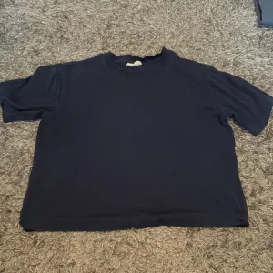 Mörkblå t-shirt från Gina Tricot - En enkel och chill mörkblå t-shirt från Gina Tricot, perfekt för dig som gillar basic vibes. Modellen är rak med rund hals och korta ärmar. Materialet är mjuk bomull som känns skönt mot huden. Passar dig som vill ha en clean och avslappnad stil.