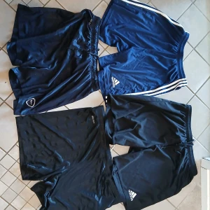 4-pack sportshorts från Adidas & Nike - Fyra par sportiga shorts i svart och mörkblått från Adidas och Nike. Perfekta för träning eller fotboll, med elastisk midja och snörning på vissa. Adidas-shortsen har klassiska ränder och logga, Nike har Dri-Fit-teknologi. Snygga och bekväma för aktiva dagar. 80 kr styck,Hör av dig om frågor. 