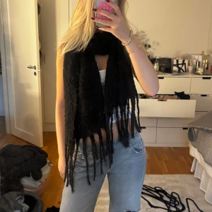 Svart lång halsduk med fransar - Säljer en svart, superlång halsduk med grova fransar i ändarna. Den är stickad och har en chunky look som gör den riktigt mysig och cool. Perfekt att svepa runt halsen för extra värme och stil under kalla dagar.