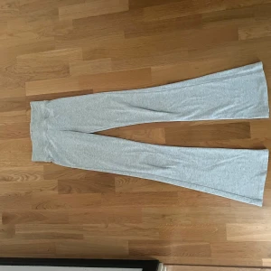 Grå bootcut mjukisbyxor från Bershka - Supermjuka ljusgrå mjukisbyxor från Bershka med bred ribbad hög midja och bootcut-ben. Perfekta för chill dagar och har en skön passform som sitter snyggt över höfterna. Materialet är stretchigt och bekvämt.