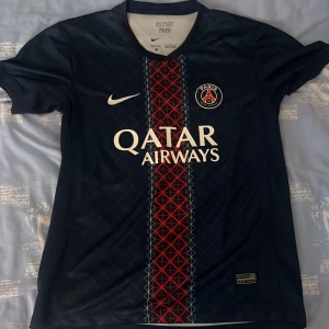 PSG Dembele 10 matchtröja Nike - Paris Saint-Germain fotbollströja med Ousmane Dembélé och nummer 10 på ryggen. Mörkblå med röd och vit rand i mitten, PSG-emblem och Nike-logga på bröstet. Qatar Airways sponsortryck. Tillverkad i lätt och ventilerande material.