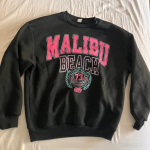 Svart sweatshirt Malibu Beach  - Svart sweatshirt från Shein med stort tryck i rosa och turkos text 'Malibu Beach' framtill. Tröjan har rund hals, långa ärmar och ribbade muddar. Mjuk insida och normal passform. Änvänd några fåtal gånger men ingen syn på användning