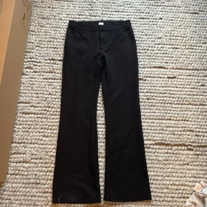 Svarta kostymbyxor från Lindex Kids i storlek 152 - Svarta kostymbyxor från Lindex Kids i klassisk modell med raka ben och hällor för bälte. Byxorna har fickor fram och dekorfickor bak, perfekt för en clean och stilren look. Materialet känns mjukt,öljsamt och skönt