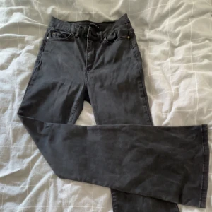 Svarta bootcut jeans med medel midja - Snygga svarta jeans med bootcut-modell och medel midja. Jeansen har klassiska fem fickor, bälteshällor och dragkedja med knapp. Materialet är mjukt och stretchigt för en bekväm passform. Perfekta för dig som gillar en tidlös och trendig look.