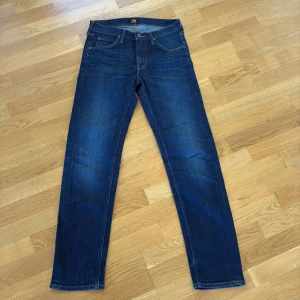 Mörkblå Lee jeans straight fit - W29L32 - Snygga mörkblå jeans från Lee med klassisk femficksdesign och raka ben. Jeansen har Lee-logga på bakfickan och är tillverkade i slitstarkt denimtyg. Perfekt passform med normal midja och subtila slitningar för en cool look. Som nya. Inga synliga tecken på användning. 