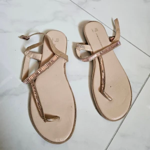 Beige sandaler med glittriga detaljer - Snygga beige sandaler från Atmosphere med tunna remmar och glittriga pärldetaljer längs ovansidan. Platt sula och öppen tå gör dem perfekta för varma dagar. Stängs med ett smalt spänne runt ankeln.