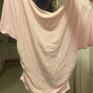 Ljusrosa topp från Gina Tricot - Supersöt ljusrosa topp från Gina Tricot i storlek S. Toppen har korta ärmar, draperad effekt i sidorna och en lösare passform. Tillverkad i mjukt, stretchigt material som känns skönt mot huden. Perfekt för dig som gillar en enkel men ändå trendig look.