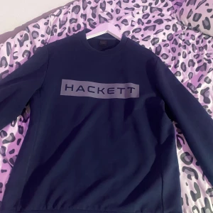 Mörkblå sweatshirt från Hackett London - Säljer en stilren mörkblå sweatshirt från Hackett London Sport i storlek M. Tröjan har rund halsringning, långa ärmar och en stor logga framtill. Perfekt för dig som gillar enkel och sportig stil. Oanvänd!