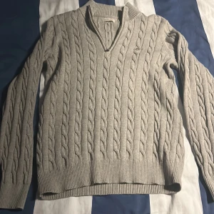 Beige kabelstickad tröja Gant - Kabelstickad beige tröja från Gant med en halvzip . Klassisk design med lång ärm och diskret logga på bröstet. Perfekt för lager-på-lager och snygg till jeans eller chinos. Använd 2 gånger priset är inte satt i sten