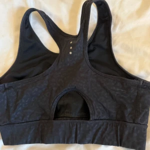 Svart sport-bh från Stronger med leopardmönster - Sport-bh från Stronger i svart med diskret leopardmönster. Modellen har brottarrygg, bred resår nedtill och en cool cut-out detalj på ryggen. Perfekt för träning och ger en snygg och sportig look.