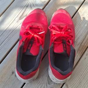 Röda Nike sneakers med svart swoosh - Säljer ett par röda Nike sneakers med svart swoosh på sidorna. Skorna har snörning, mesh-ovandel och en vit, dämpad sula med svart yttersula. Perfekta för träning eller vardagsstil. Snygg och sportig look med bekväm passform.