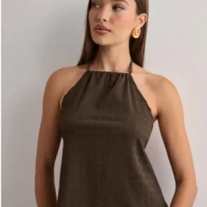 Beun topp öppen i ryggen - Säljer en brun topp med snygg snörning i nacken. Toppen har en cool struktur i tyget och är ärmlös med halterneck. Perfekt för dig som gillar stilrena och trendiga plagg med lite edge. Aldrig använd