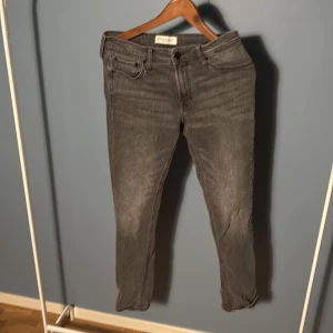 Grå jeans från Stock & Hank W31 L32 - Snygga grå jeans från Stock & Hank i klassisk femficksmodell. Jeansen har en smal passform och raka ben, med diskret tvättad look och svarta detaljer vid knappar. Perfekta för dig som gillar stilrena och enkla jeans i vardagen.