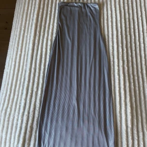 Grå långklänning med smala ränder - Säljer en stilren glittergrå långklänning med smala svarta och vita ränder. Klänningen är ärmlös och har en rak, enkel passform. Materialet känns mjukt och stretchigt